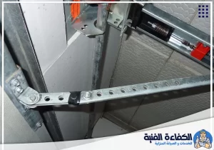 معاينة ذراع التثبيت والوصلات المعدنية لتحديد أسباب تعطل آلية فتح وإغلاق باب الكراج قبل الإصلاح.